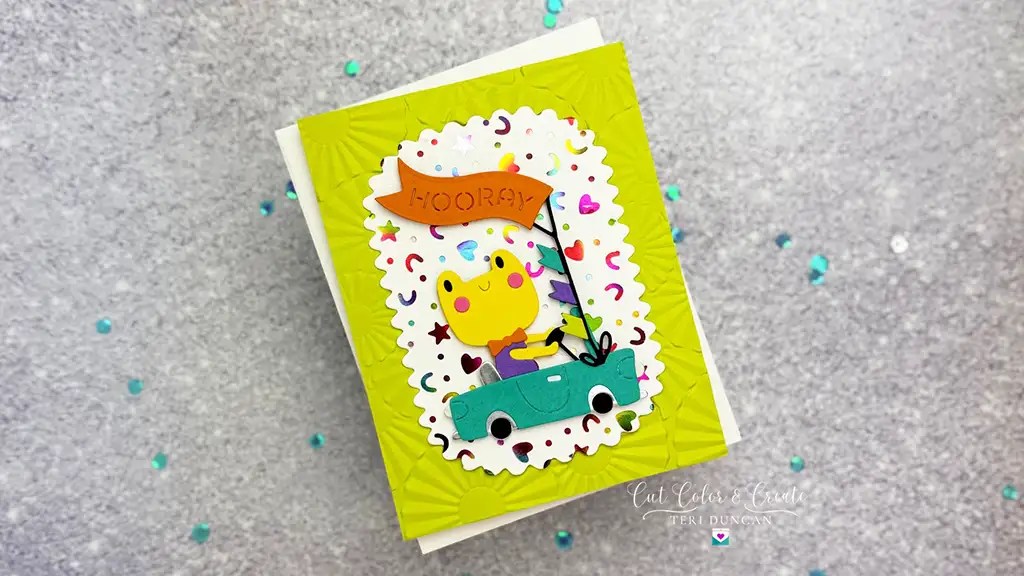 Greeting card with a cartoon character in a car holding an orange "Hooray" flag, set on a confetti-patterned background with a lime green border made using November 24 Club Ki.