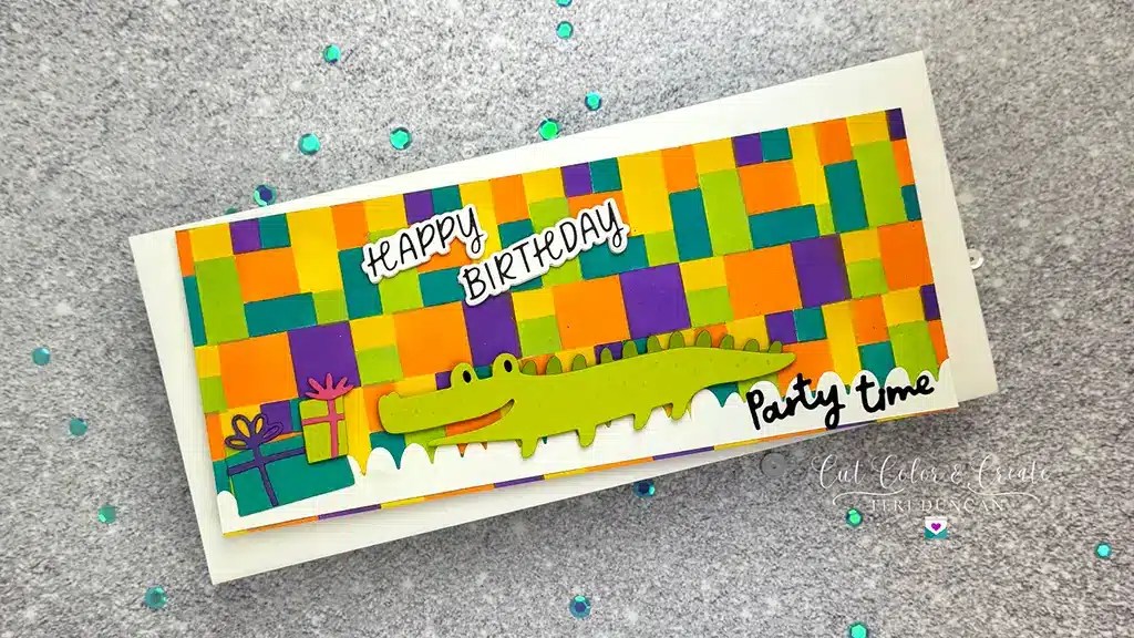Colorful birthday card with a green crocodile, presents, and “Happy Birthday” and “Party Time” text against a multicolored checkered background. Blue and turquoise confetti scattered around made using November 24 Club Ki.