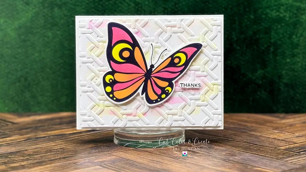 A handmade thank you card features a colorful butterfly on an embossed white background with a woven pattern, crafted 3D Embossing Folder and Betterpress January '25 Club Kits from Spellbinders, set against a green backdrop.