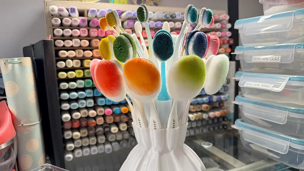 Colorful makeup brushes with oval heads in a holder, set against a backdrop of organizing drawers and storage boxes—perfect for those seeking craft room organization inspiration.