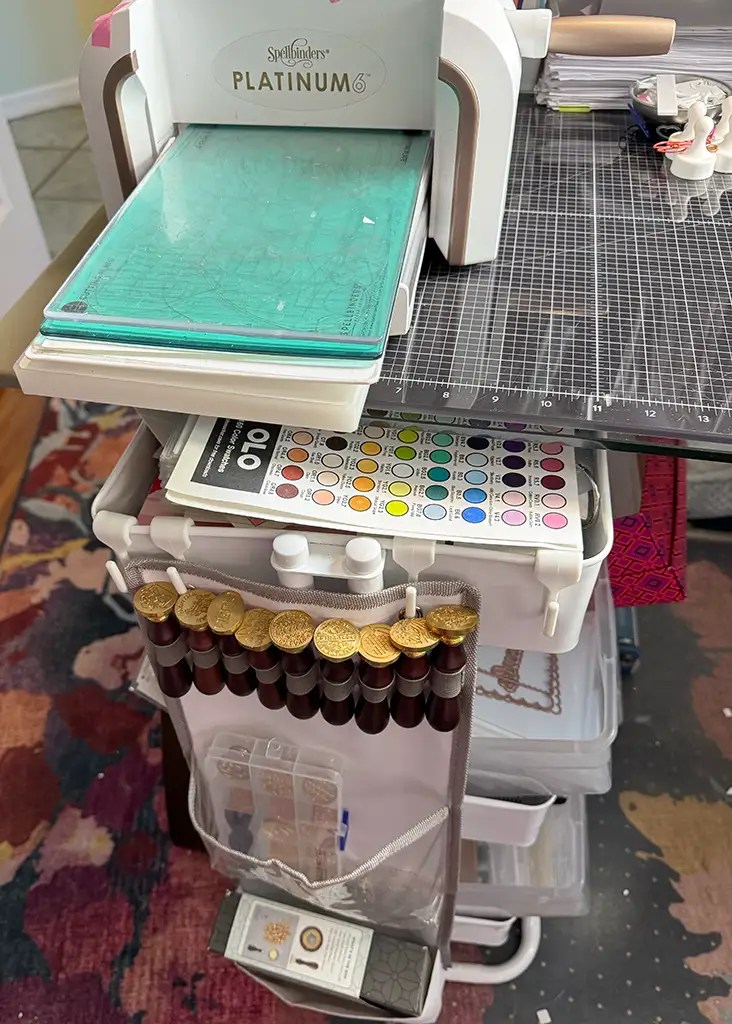 Crafting station featuring a die-cutting machine, color swatches, ink bottles, and impeccably organized supplies on a cart—a model of craft room organization.