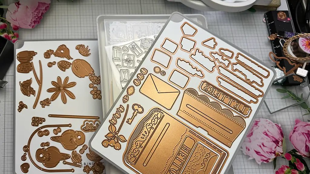 Metallic die-cutting plates featuring flowers, leaves, and envelopes are laid out on a table with some pink flowers around them, showcasing clever craft room organization hacks #1.