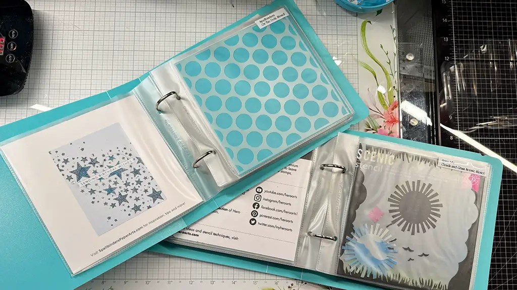 Two open binders rest on a grid surface. The left binder flaunts blue polka dot sheets, while the right showcases stencils with sunburst and star patterns—an inviting scene for any craft room organization enthusiast. Papers and labels add to these clever organization hacks.