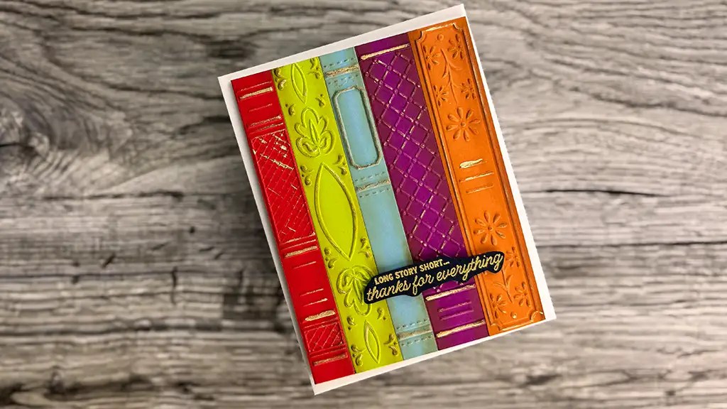 A colorful greeting card with embossed spines resembling books and a label that reads, "Long story short, thanks for everything," perfect for card making or including in your May '25 Club Kits, placed on a wooden surface.