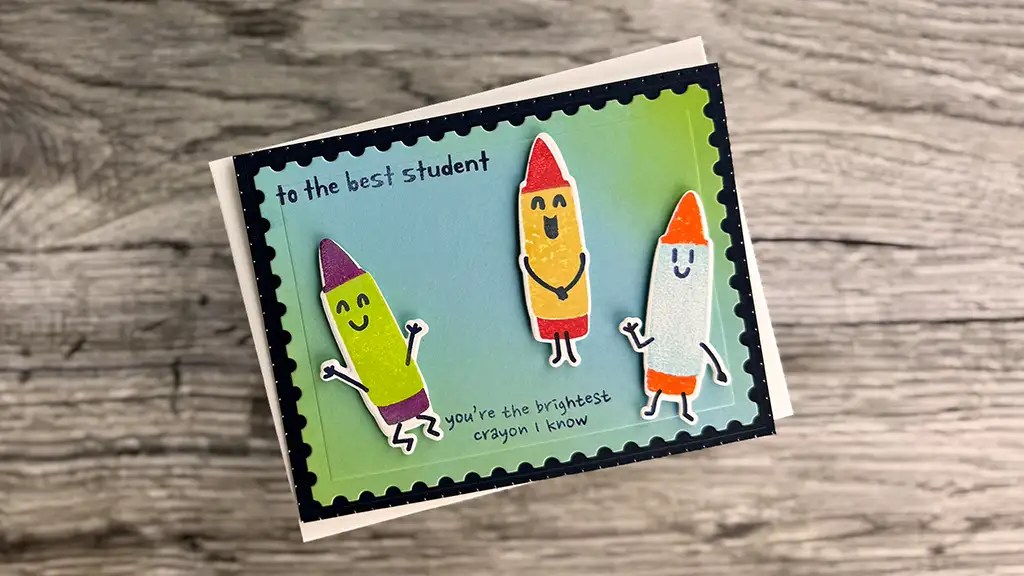 A handmade card from our May 25 Club Kits features three smiling cartoon crayons and the text "to the best student" and "you're the brightest crayon I know" on a green and blue background—perfect for card making enthusiasts.