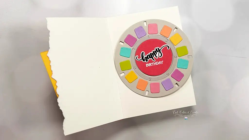An open greeting card with a circular viewfinder reel design inside, colorful squares around the edge, and "Happy Birthday" written in the center—perfect for inspiring your own note cardmaking ideas. Created with products from Spellbinders' Take A Note collection.