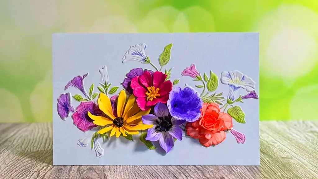 A stunning card, handmade with colorful 3D flowers and green leaves, is displayed on a wooden surface with a blurred green background—perfect for celebrating the summer solstice.