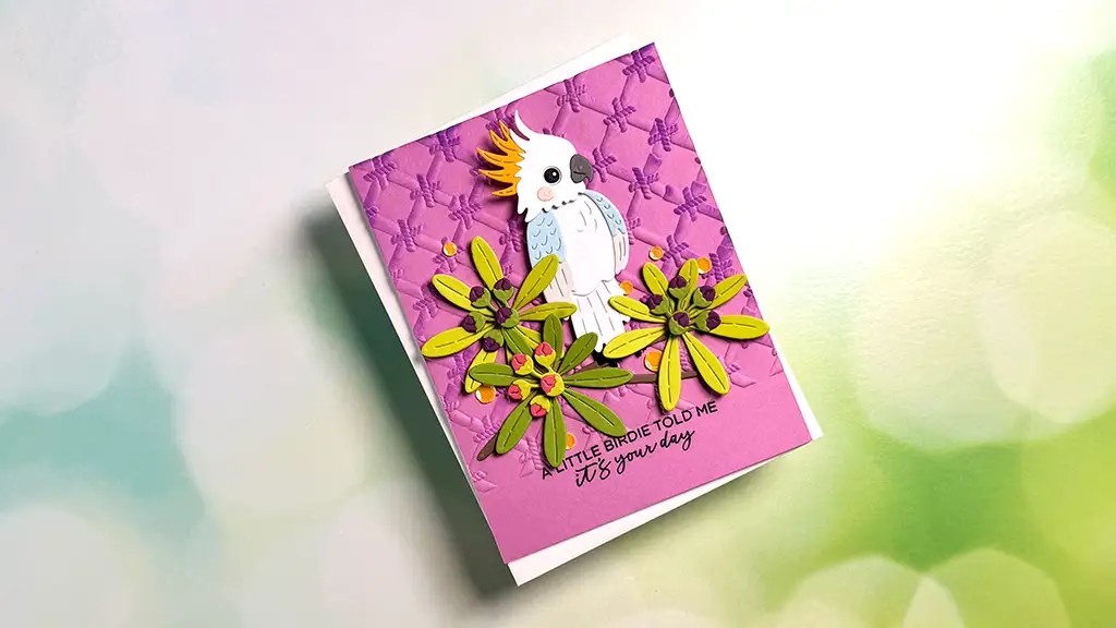 A handmade greeting card from the Gorgeous Cards collection, with a 3D white cockatoo, yellow flowers, and a purple textured background, featuring the cheerful chirp: “A little birdie told me it’s your day.”.