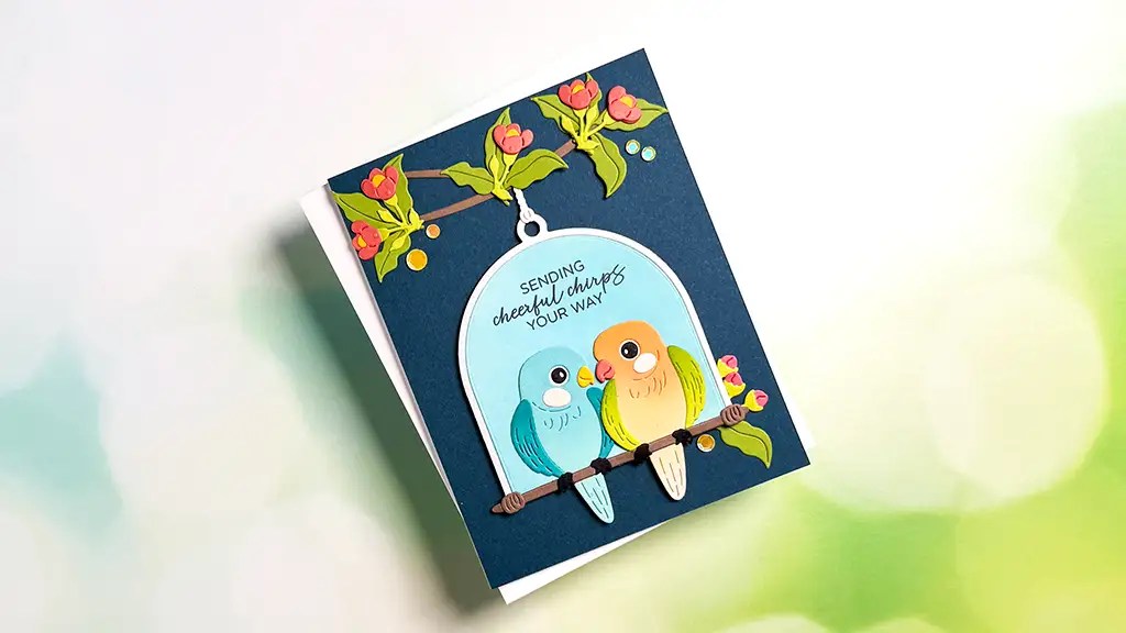 A gorgeous card featuring two colorful birds on a branch, floral accents, and the message “Sending Cheerful Chirps your way” on a dark background—perfect for cardmaking enthusiasts.