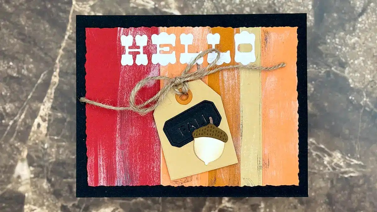 A handmade greeting card with "HELLO" in white letters, autumn-colored stripes, and a tag tied with twine featuring an acorn and the word "FALL" on a black label—perfect for your Autumn Archives or inspiring new Fall Card Ideas.
