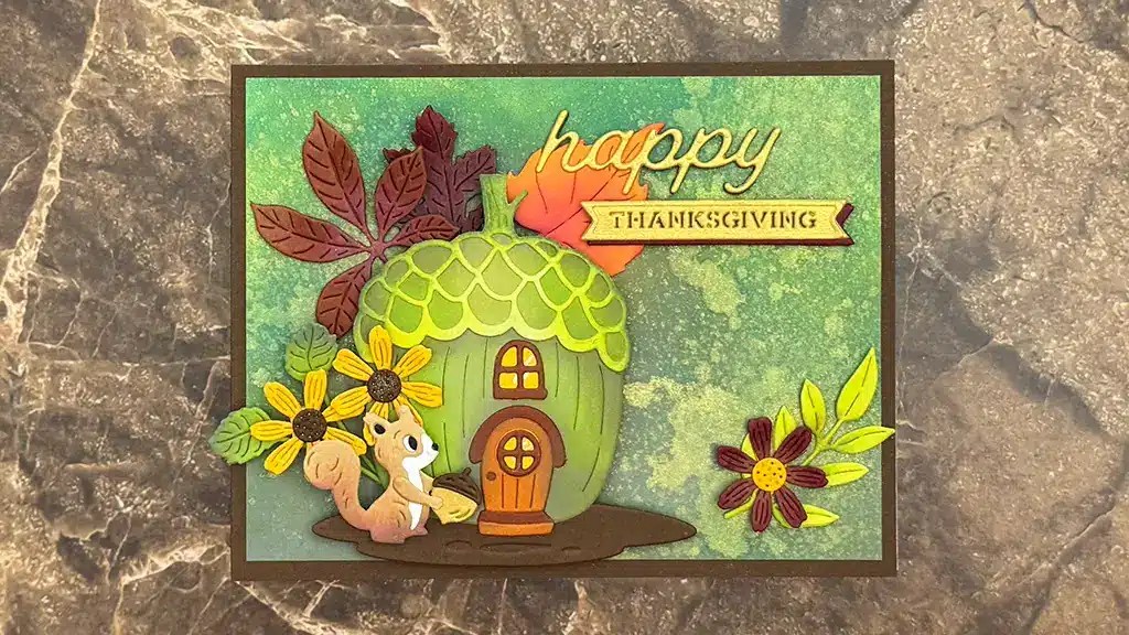 Handmade card featuring a squirrel, a green acorn house, flowers, autumn leaves, and the text "happy Thanksgiving" on a green textured background. This card was created using Spellbinders' Sept 25 Club Kits Large Die of the month Acorn Acres.