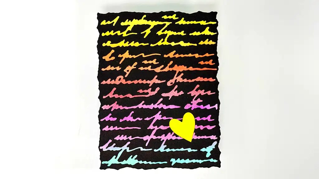 A piece of black paper with colorful cursive writing and a yellow heart shape near the bottom right corner.