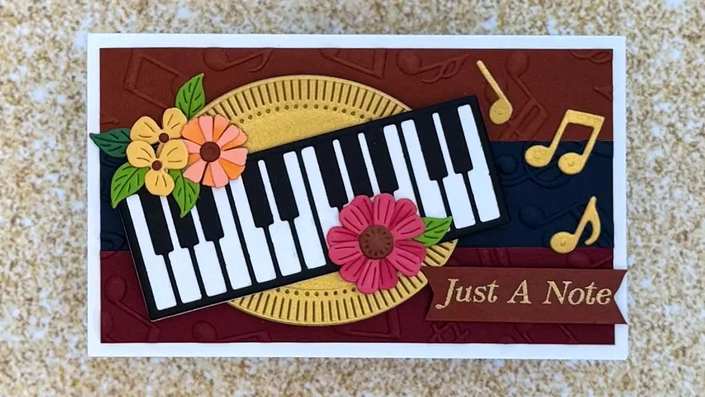 Handmade Music-Themed Greeting Card featuring a piano keyboard, colorful paper flowers, musical notes, and the phrase "Just A Note" on a decorative background. Perfect for music lovers!.