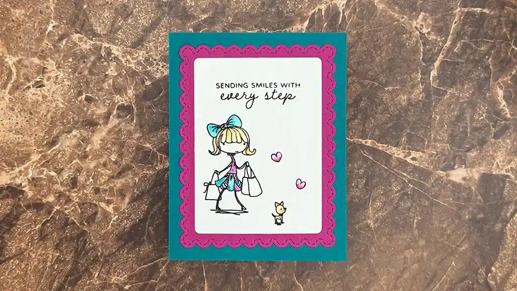 A greeting card on a marble surface shows a cartoon girl with shopping bags, a cat, and pink hearts. Featuring Spellbinders Nov 2025 Kits, the card reads: "Sending smiles with every step.