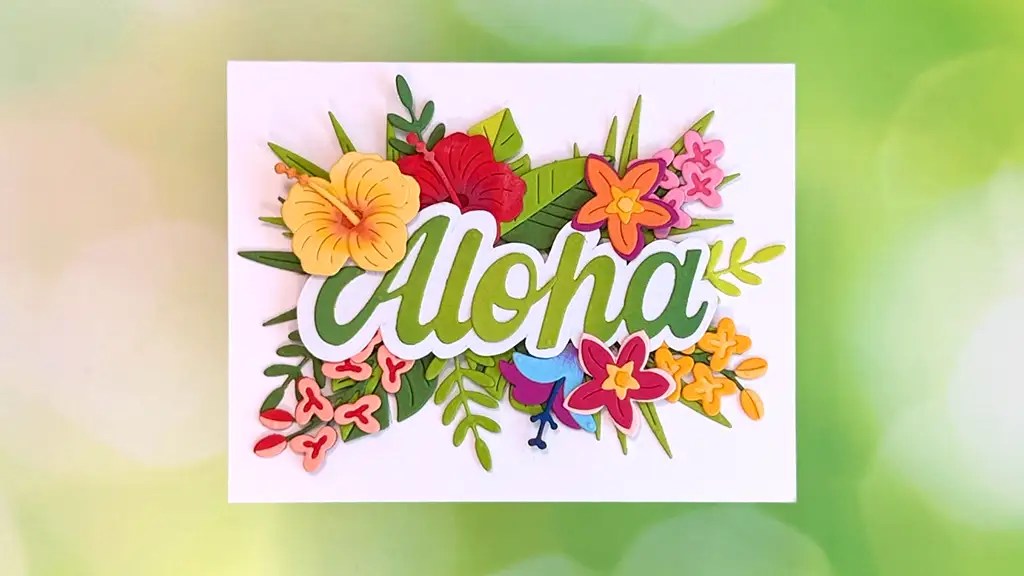 A colorful card from spellbinders paper arts june 26 clubs kits featuring the word aloha surrounded by bright layered paper flowers and green leaves on a light backgroundperfect inspiration for your next card making project