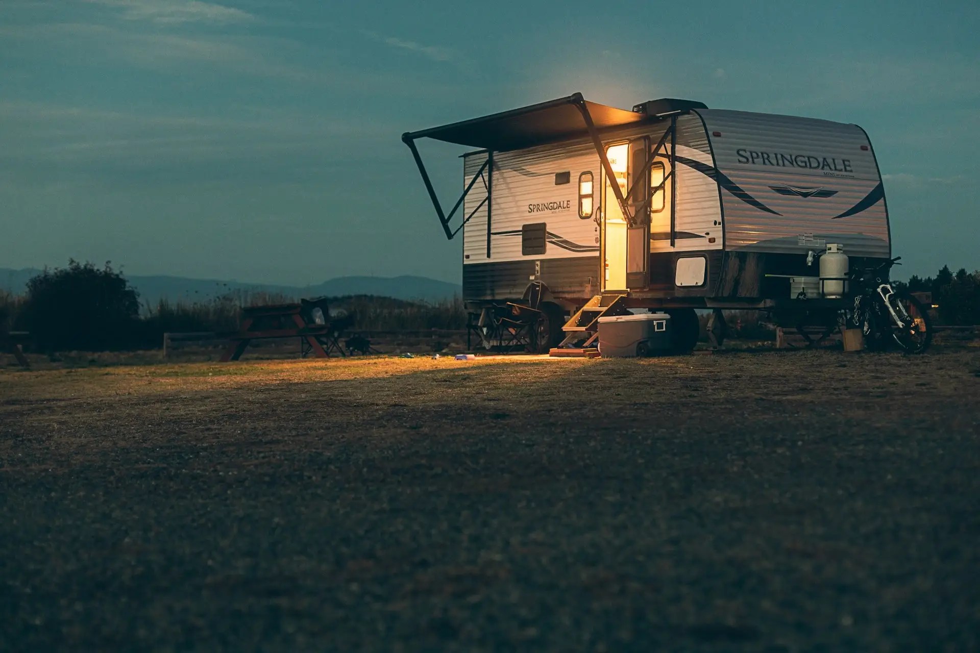 Small camper trailer parked alone in a field at dusk, symbolizing personal dependency risk and building on borrowed land