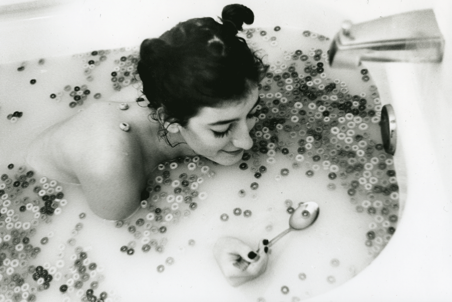 Woman in bathtub full of cereal and milk holding a spoon with cereal