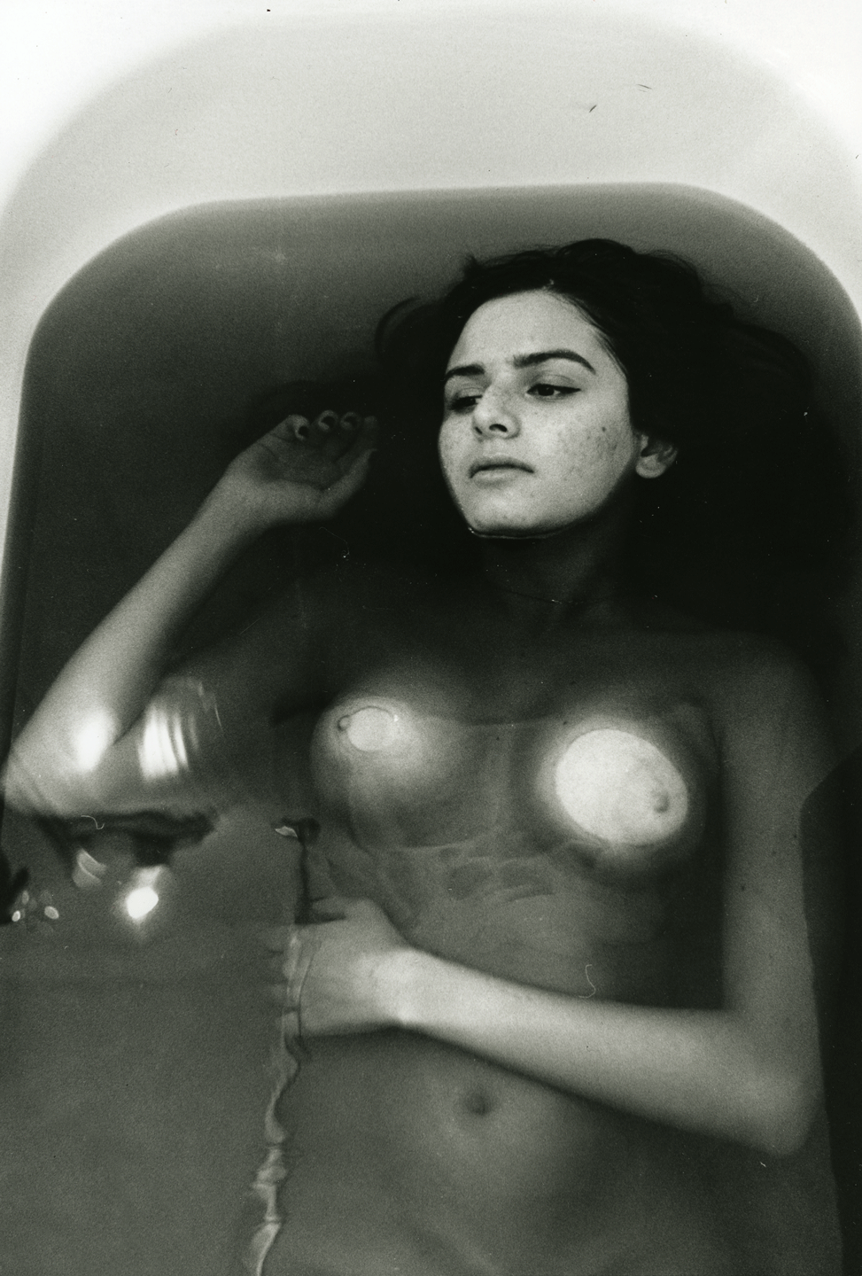 Nude woman in dark colored bath looking peaceful