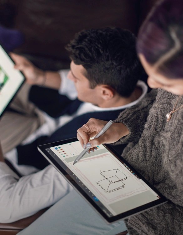 Two individuals are reviewing content on tablets, with one individual actively diagramming and/or sketching out a conceptual design with a stylus pen.