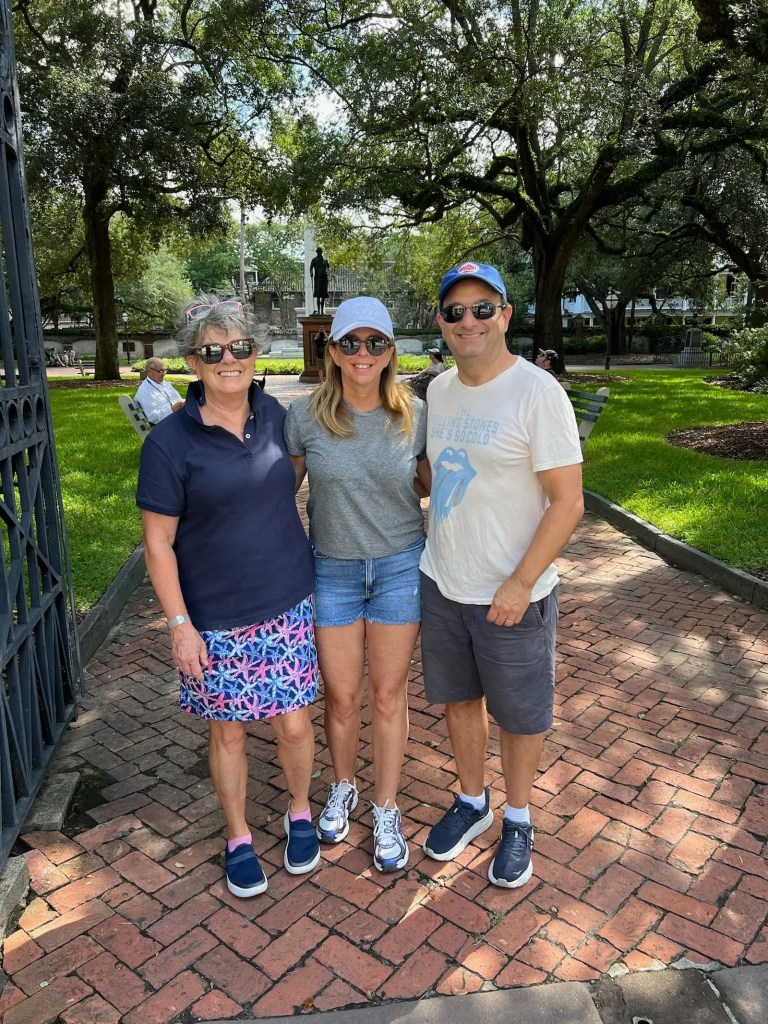 Three people standing on the brick path of Washington Square Park in Charleston, smiling with trees and a statue in the background. Alt-text generated with AI because the author is kinda lazy.