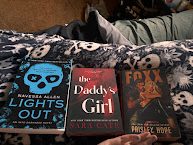 Three books displayed on a patterned blanket: 'Lights Out' by Navarrete, 'the Daddy's Girl' by Sara Cutt, and 'Foxx' by Phoenix Hope.