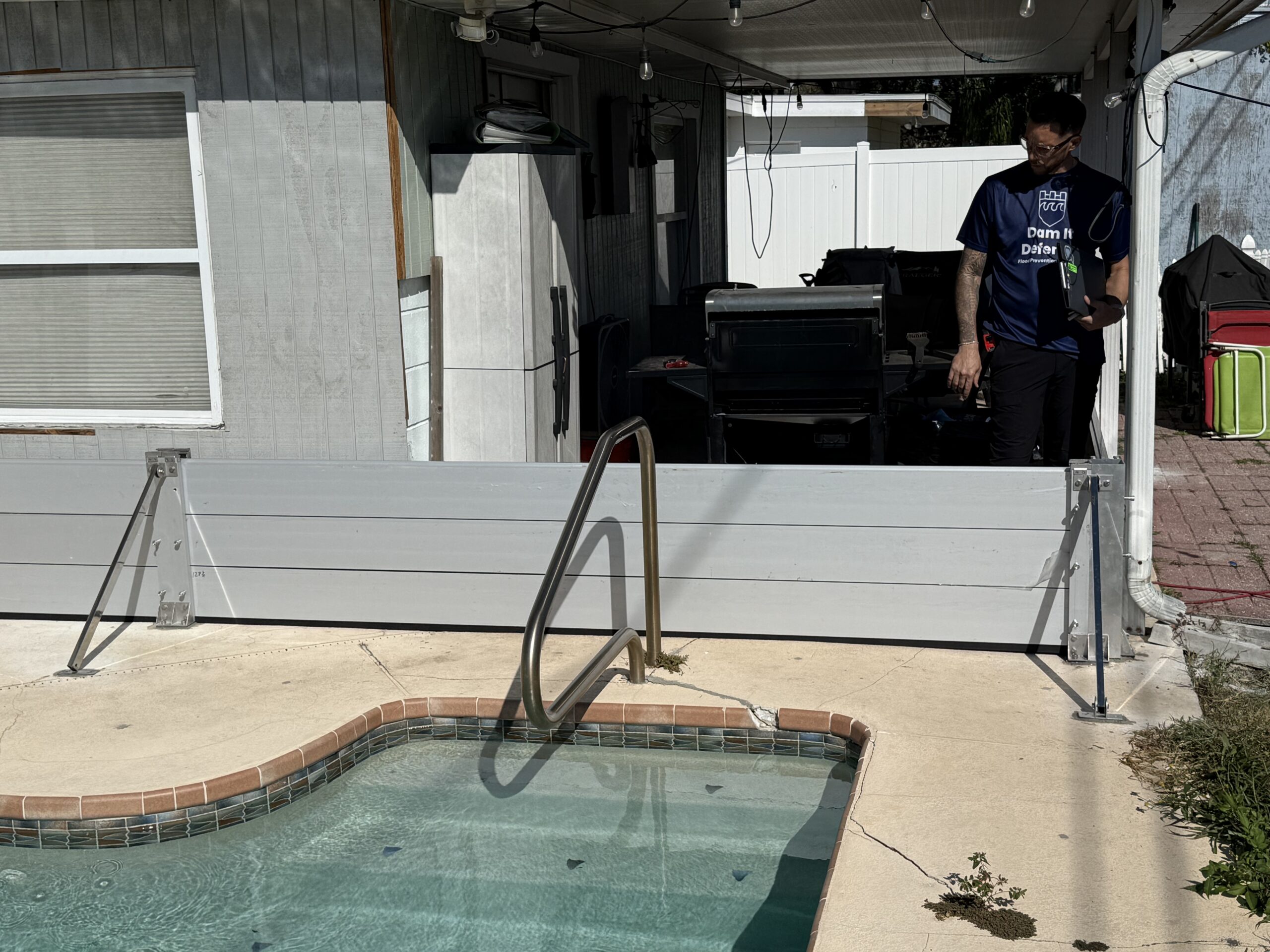 Dam It Defense installer standing behind aluminum flood barrier panels set across a pool patio opening