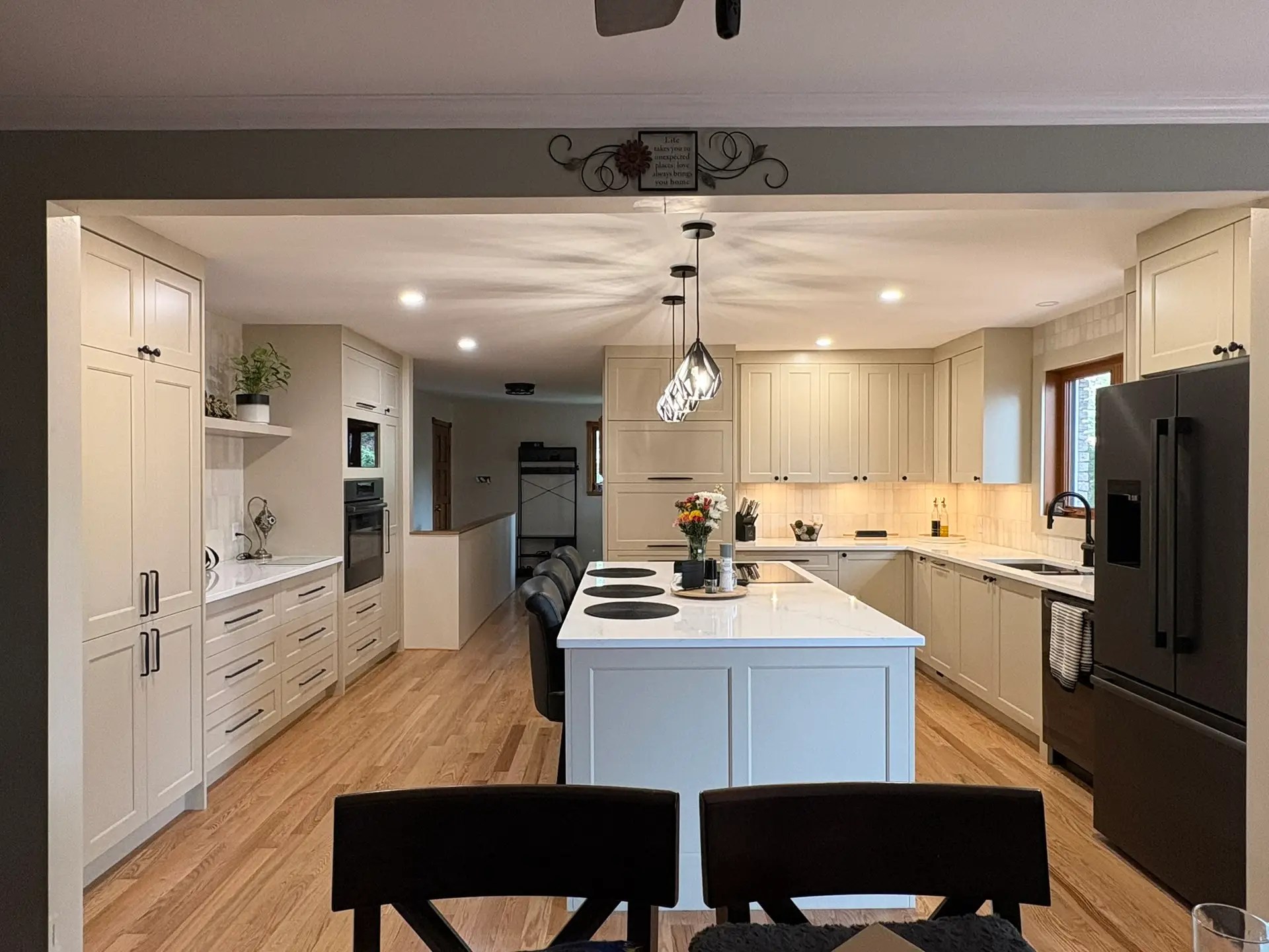 Full view of a renovated Ottawa kitchen featuring a large island with seating, in island cooktop, pendant lights, latte toned cabinetry, quartz countertops, subway tile backsplash, and natural red oak engineered hardwood floors flowing seamlessly throughout the main level.
