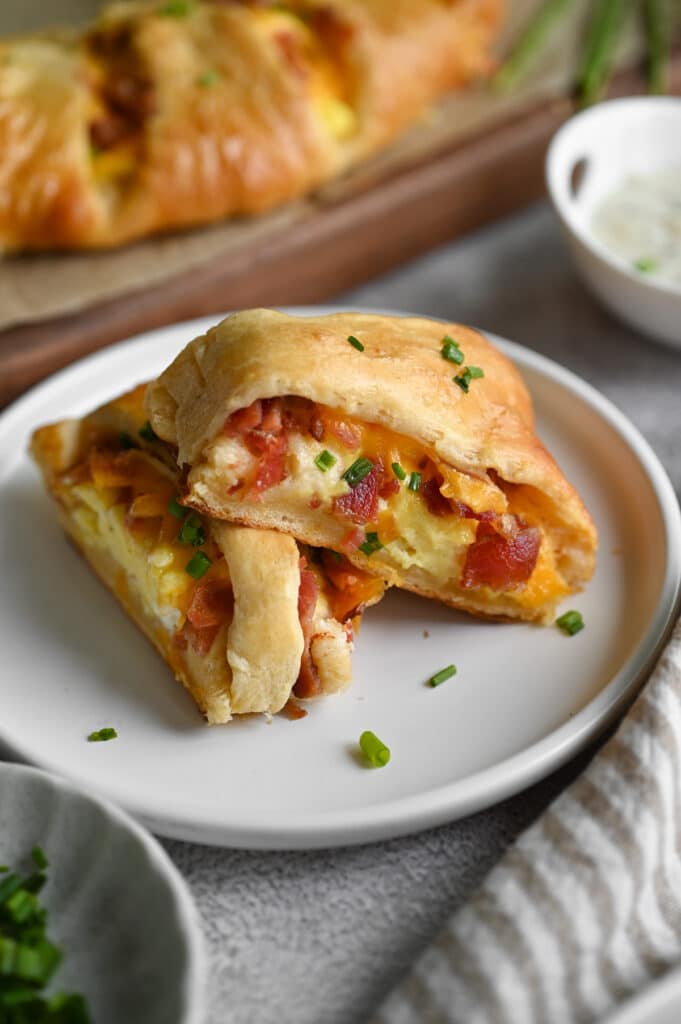 Two slices of a breakfast roll stacked on a matte white ceramic plate.