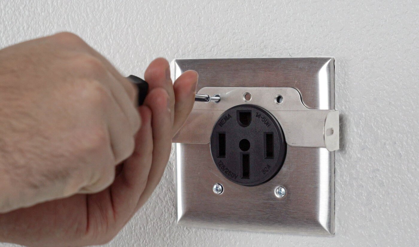 Hand installing NEMA 14-50R outlet on white wall with screwdriver.