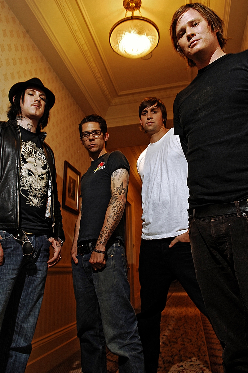 Le groupe de rock alternatif Angels & Airwaves photographié en contre-plongée dans un couloir au décor rétro, éclairage chaud et ambiance posée.