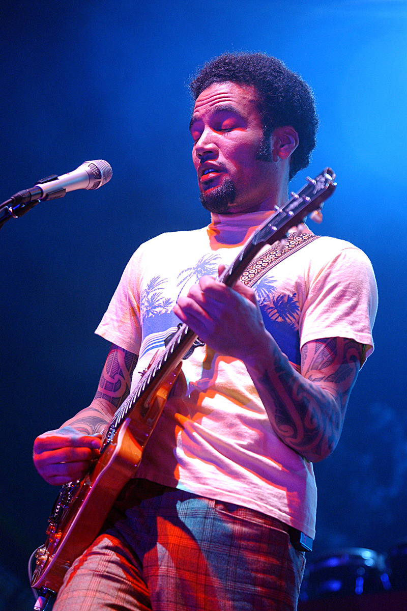 Ben Harper sur scène à Bercy, jouant de la guitare électrique sous un éclairage bleu et rose, concentré et expressif.