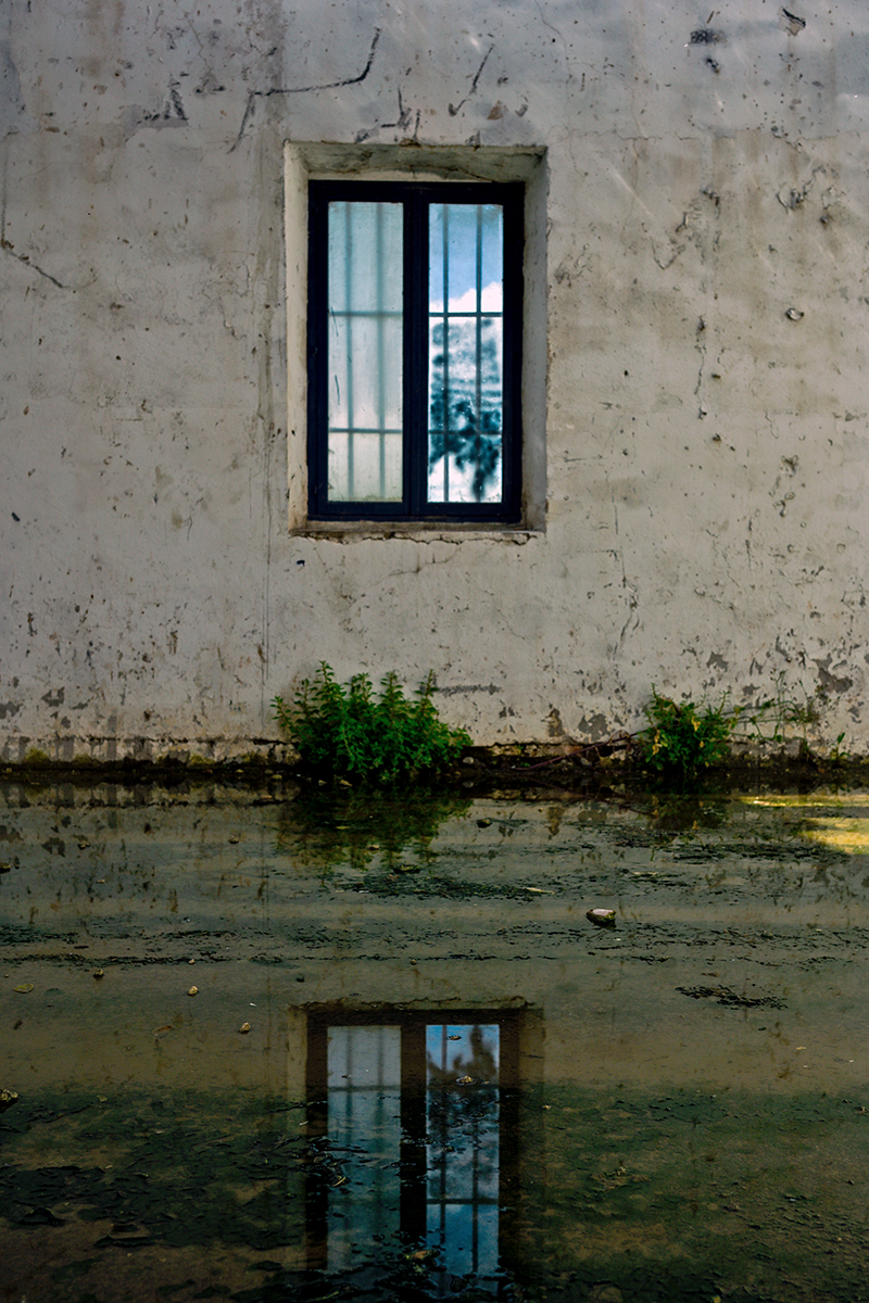 Jeu de lumière dans un entrepôt en rénovation à Béziers, avec des motifs géométriques projetés par une fenêtre à barreaux.