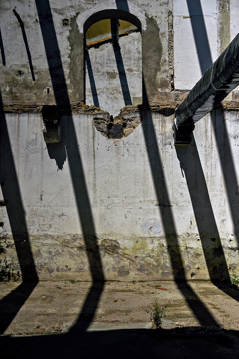 Jeu de lumière dans un entrepôt en rénovation à Béziers, avec des motifs géométriques projetés par une fenêtre à barreaux.