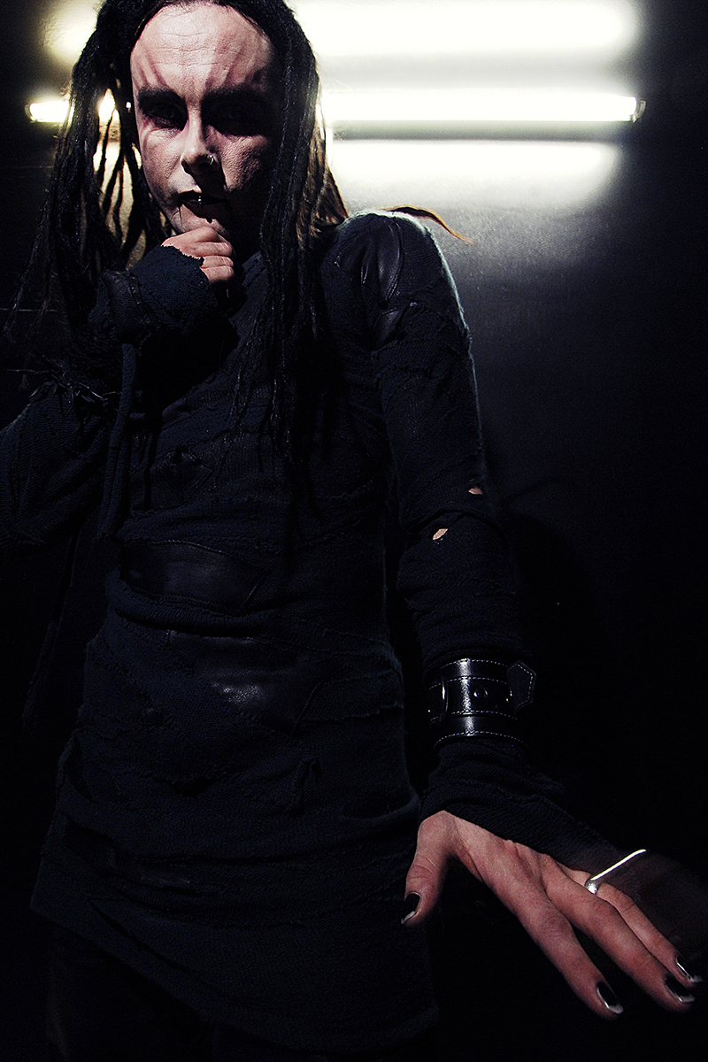 Portrait d’un membre de Cradle of Filth en tenue noire déchirée, maquillage expressionniste et lumière crue en contre-plongée