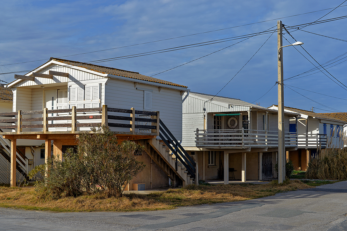 Chalets en bois à Gruissan avec des escaliers extérieurs sous un ciel bleu.