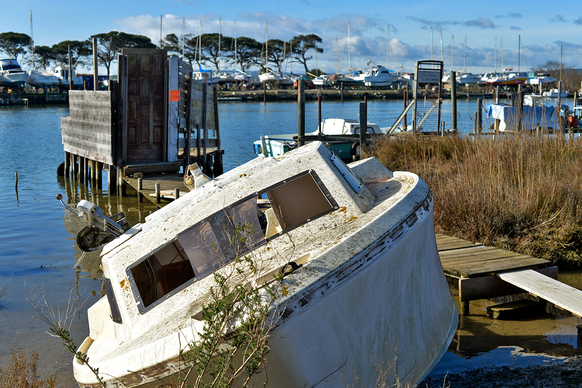 Bateau abandonné près de l'embouchure de l'Aude, avec un port de plaisance en arrière-plan.