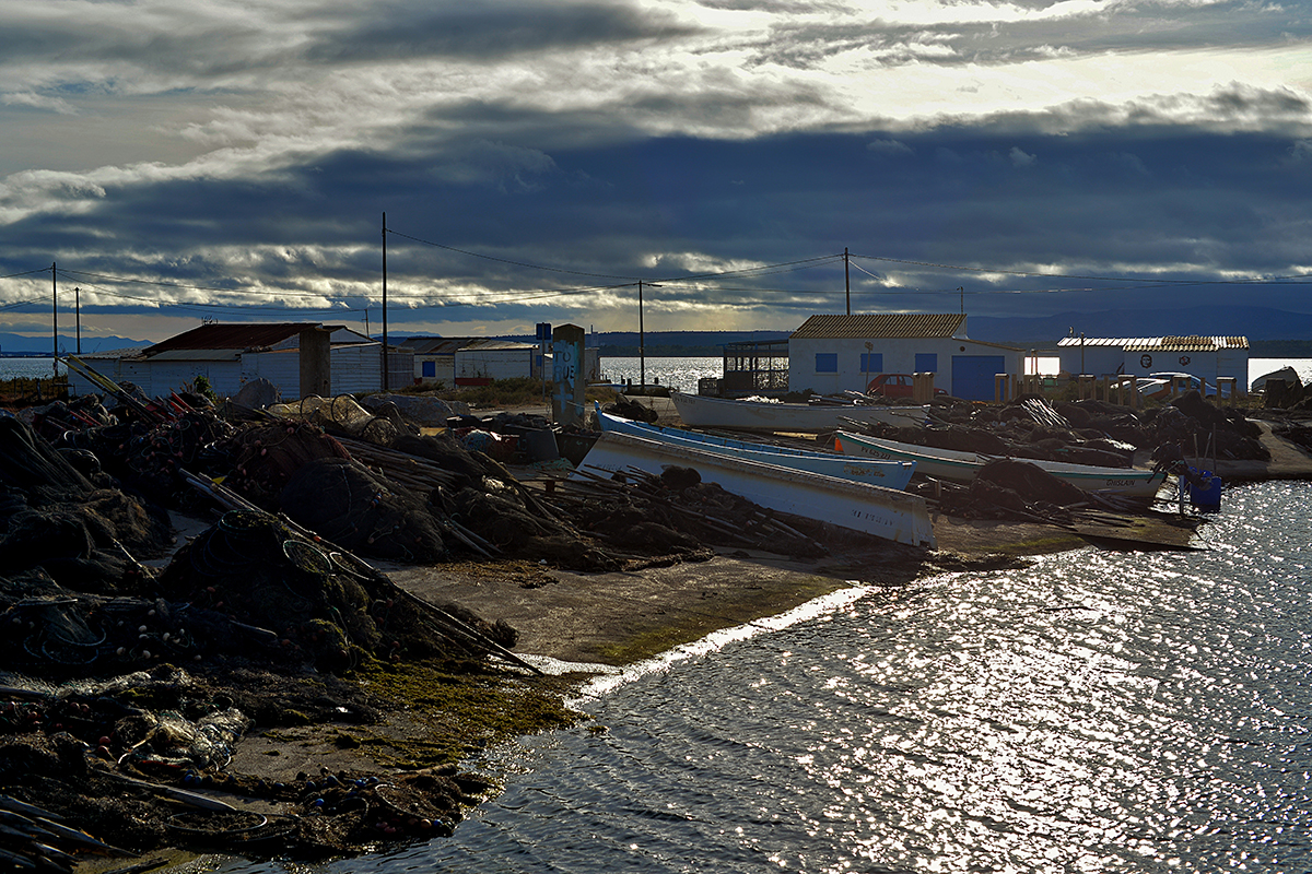 Village de pêcheurs à Gruissan avec des bateaux au repos et des maisons sous un ciel nuageux.