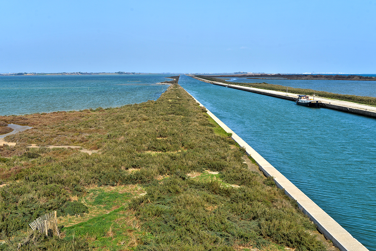 Vue aérienne du Canal du Rhône à Sète avec un bateau naviguant sur l'eau et des chemins de terre.