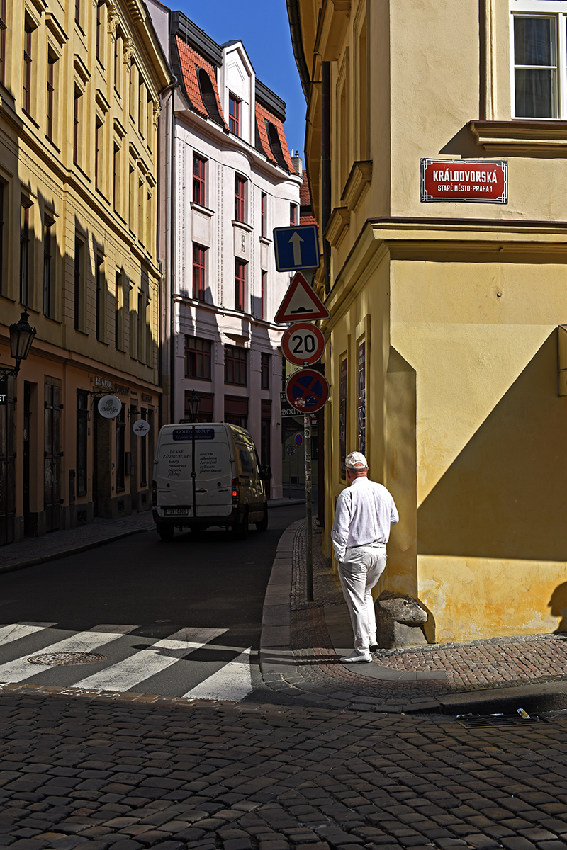 Rue étroite dans le centre de Prague avec des bâtiments colorés et une personne marchant près d'un panneau de signalisation.