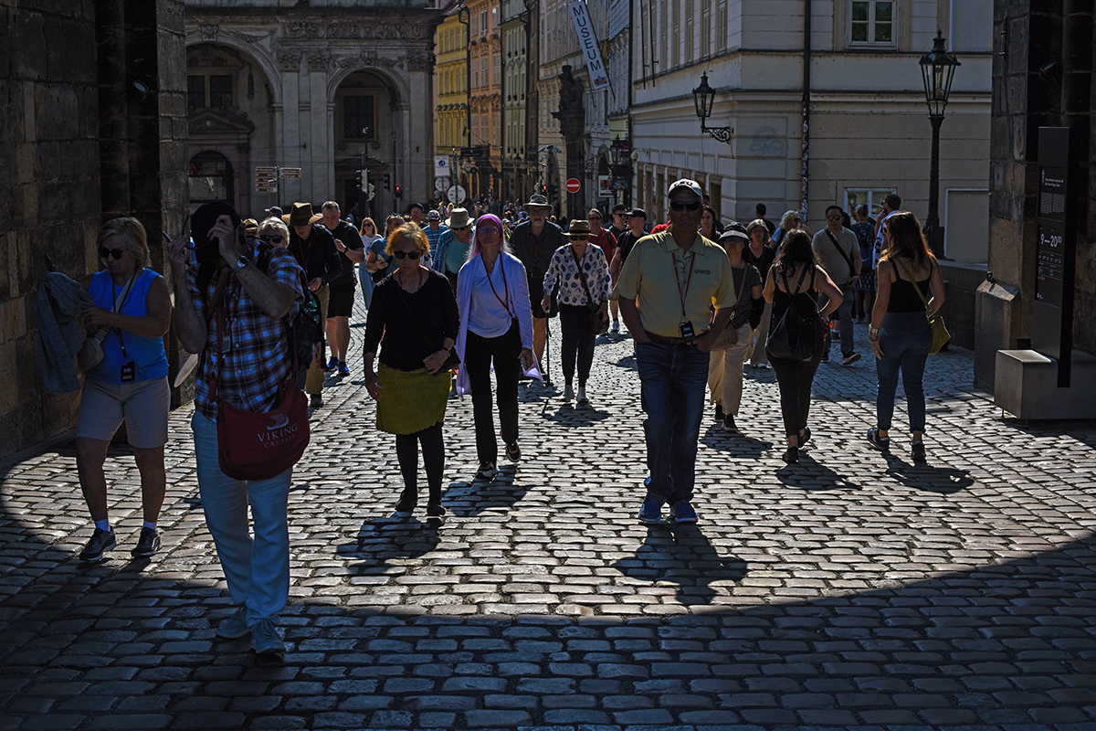 Groupe de touristes marchant vers le pont Charles à Prague, avec des bâtiments historiques en arrière-plan.