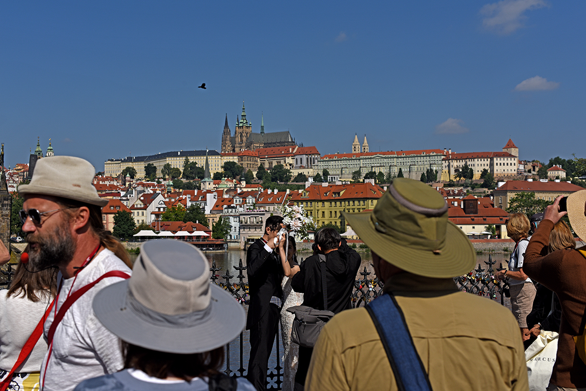 Couple de mariés s'embrassant sur le pont Charles à Prague, avec une vue panoramique sur le château de Prague et les toits de la ville.