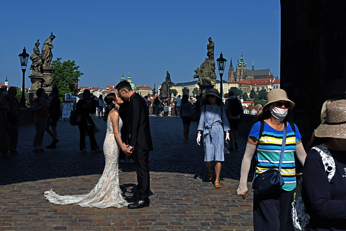 Couple de mariés s'embrassant sur le pont Charles à Prague, entouré de touristes et avec le château de Prague en arrière-plan.