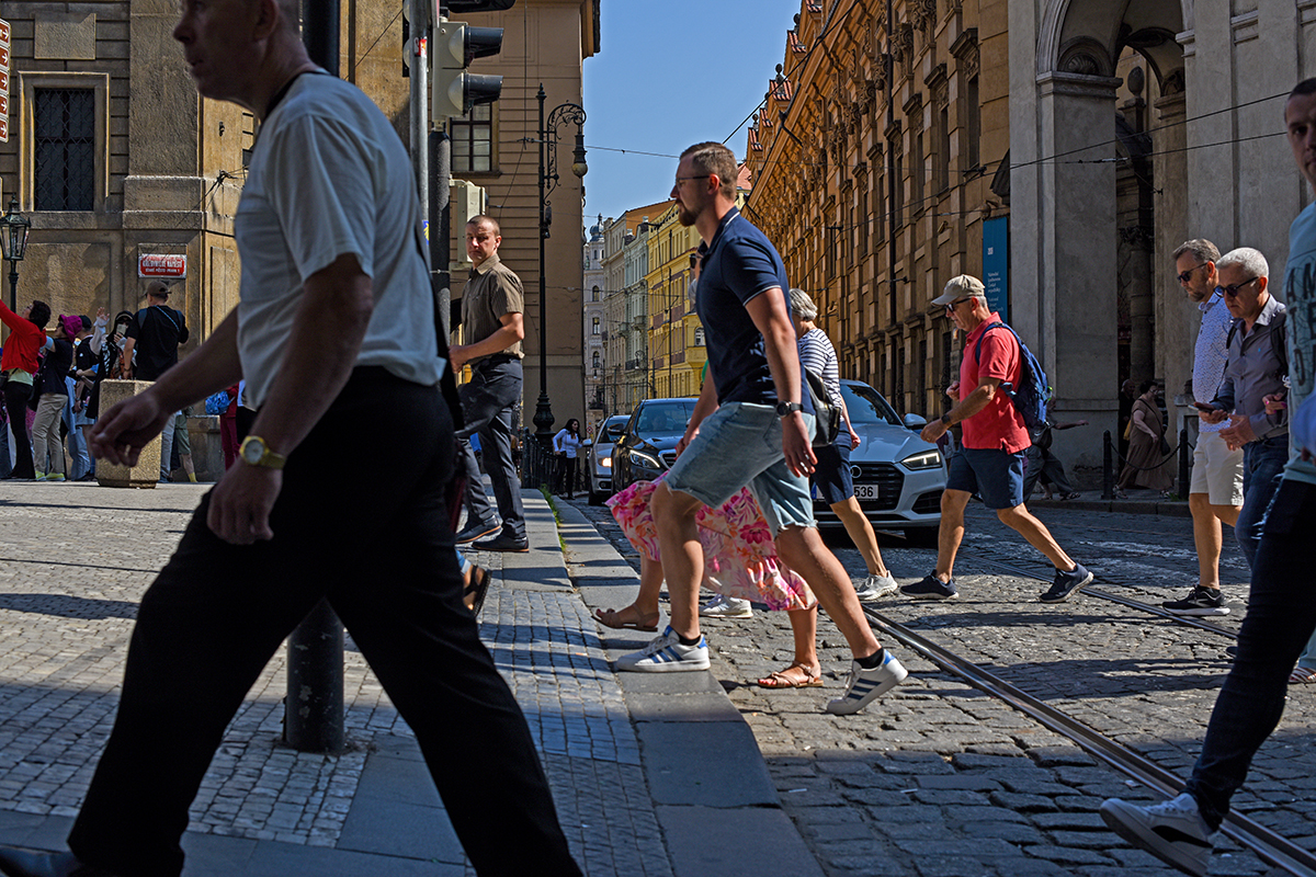 Touristes traversant une rue animée de Prague, avec des bâtiments historiques en arrière-plan.