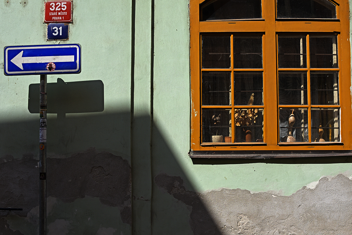 Façade d'un bâtiment dans le centre de Prague avec une fenêtre décorée et un panneau de signalisation indiquant la direction.
