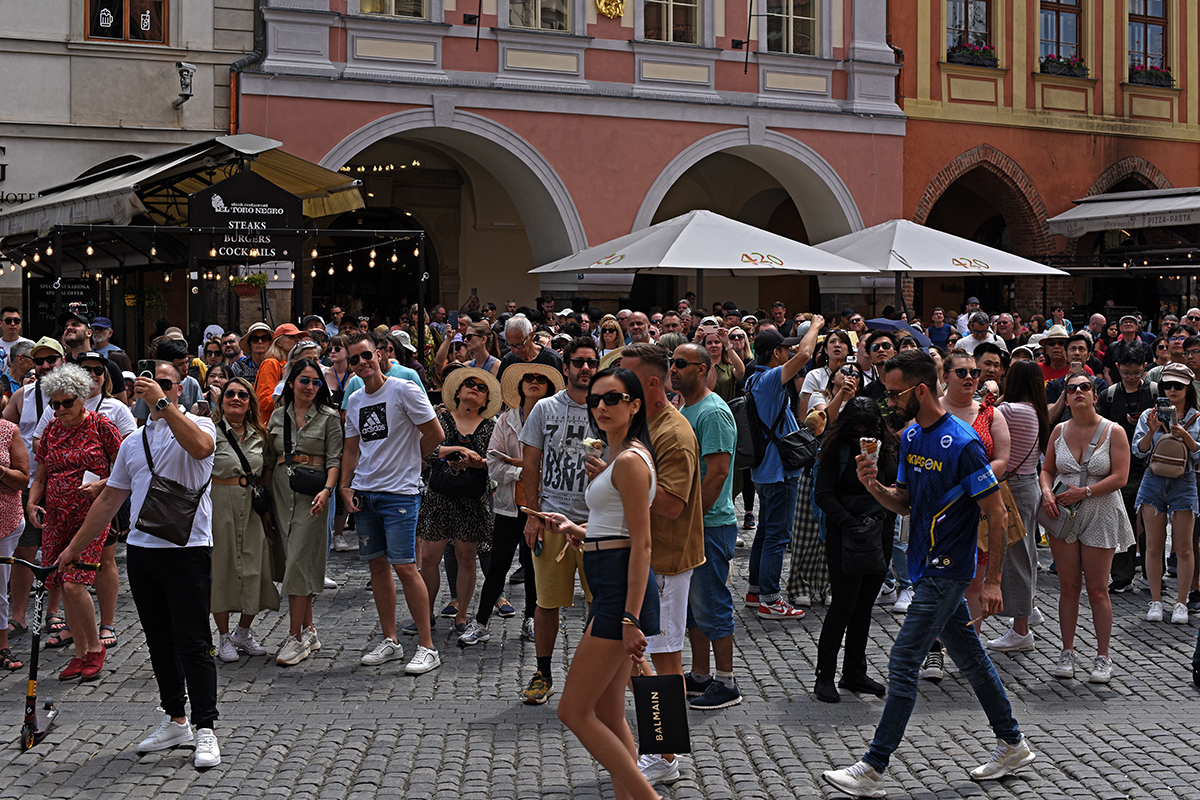 Foule de touristes dans une rue animée de Prague, avec des bâtiments colorés et des parasols en arrière-plan.