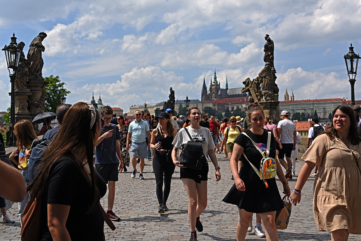 Touristes marchant sur le pont Charles à Prague, avec le château de Prague visible en arrière-plan.