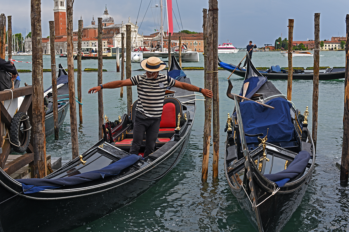 Gondolier manœuvrant une gondole sur le Grand Canal de Venise, avec d'autres gondoles amarrées à proximité.