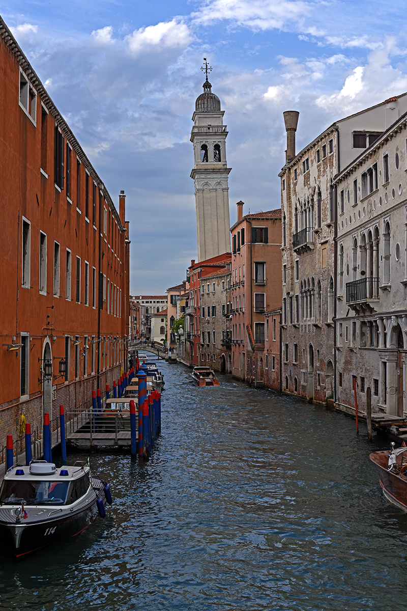 Canal de Venise bordé de bâtiments colorés et d'un clocher en arrière-plan.