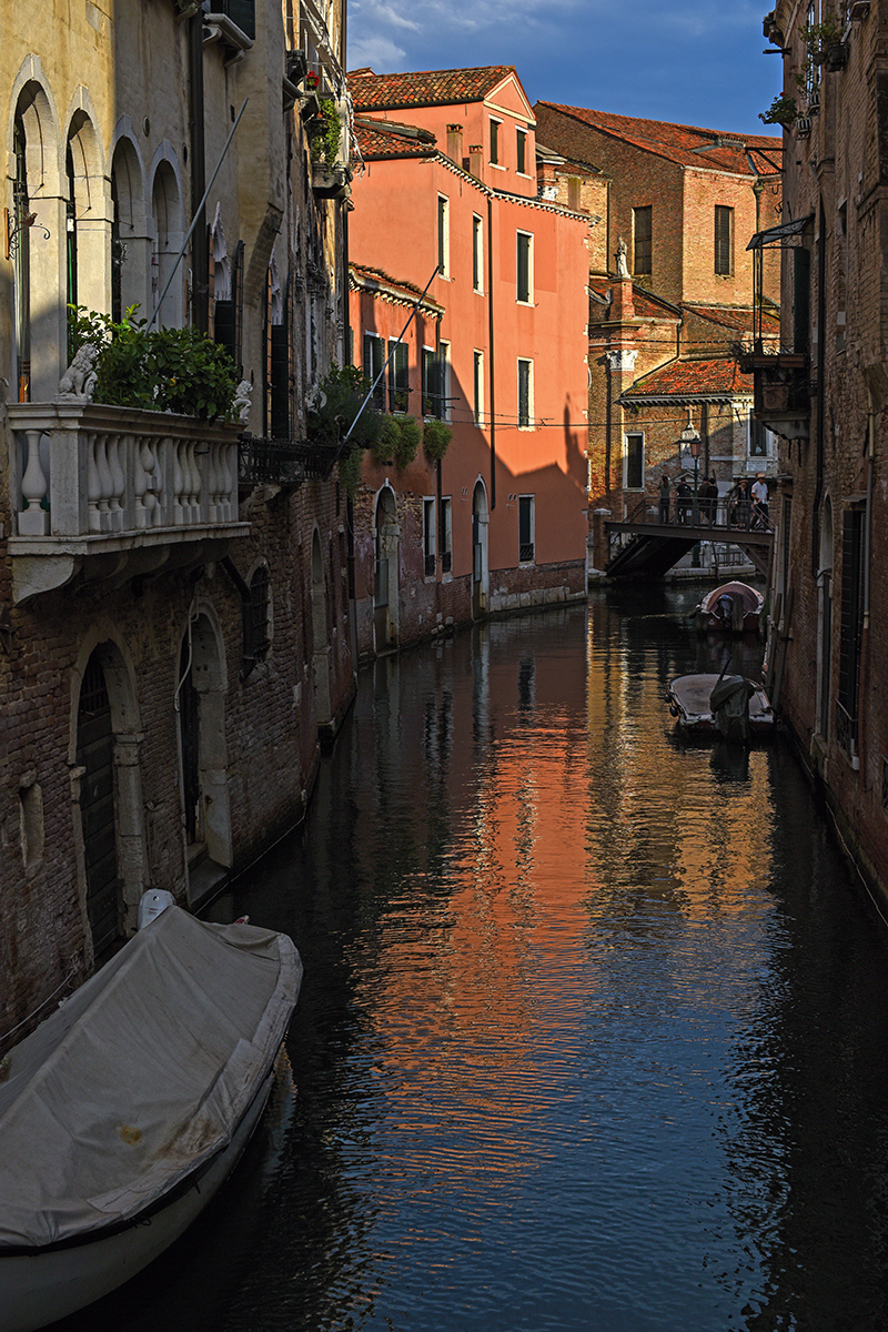 Canal de Venise avec des reflets de bâtiments colorés sur l'eau et des bateaux amarrés.