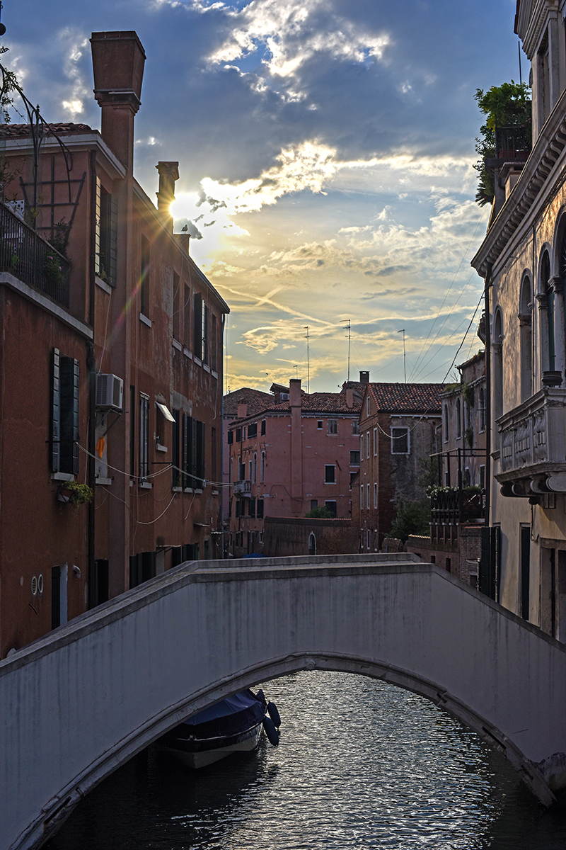 Canal de Venise au coucher du soleil avec un pont en pierre et des bâtiments colorés.